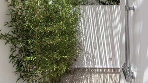 Una ducha moderna al aire libre con valla de bambú y pared blanca.