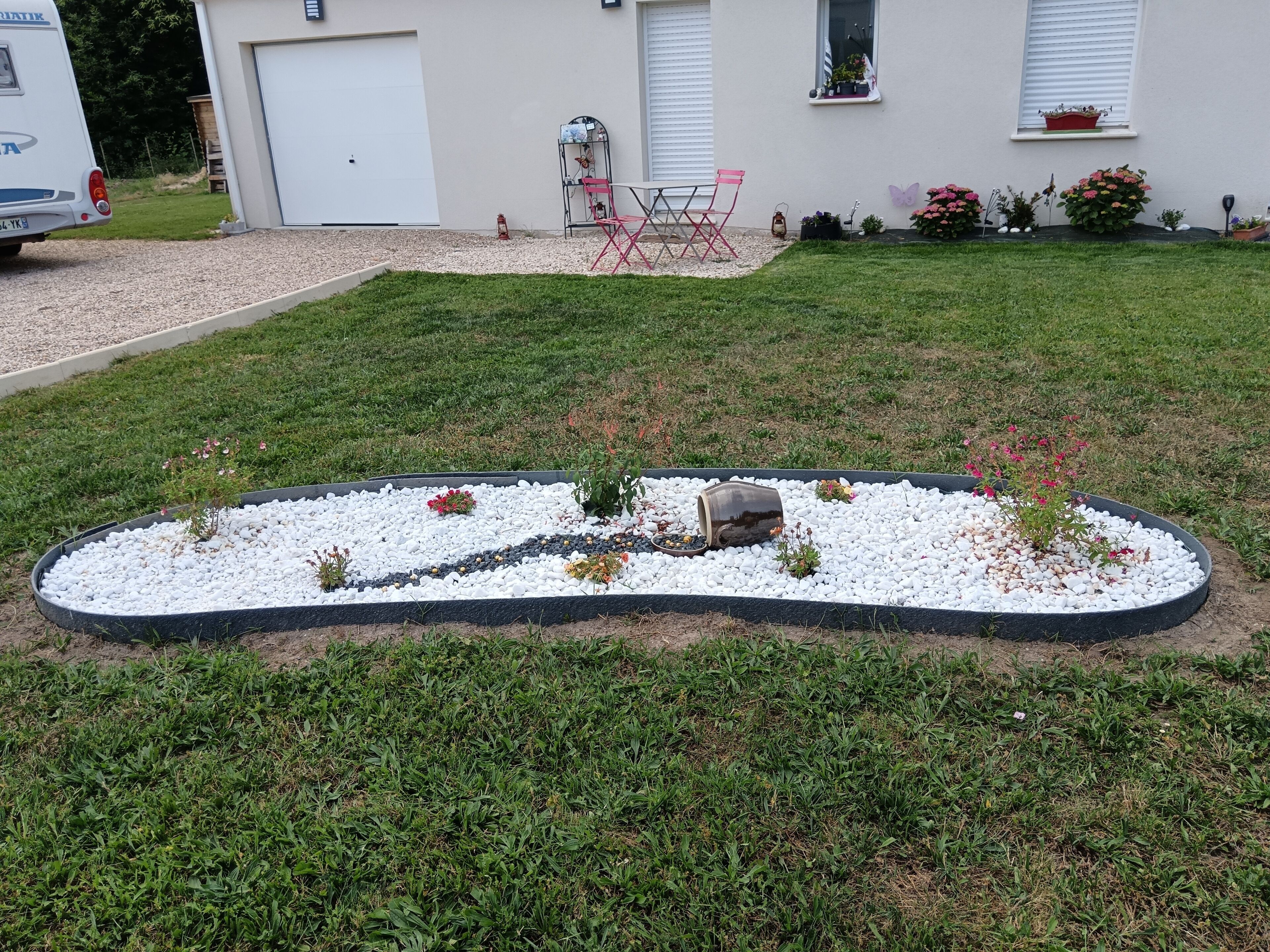 A landscaped garden with a gravel path, a small seating area, and a house with a garage and windows.
