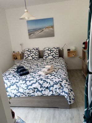 A bedroom with a bed, pillows, a bedside table, a nightstand, a lamp, a picture on the wall, and a curtain. - QUIET ROOM (Soubran)