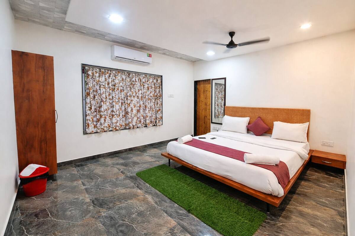 A bedroom with a bed, a ceiling fan, an air conditioning unit, a red bucket, and a green rug.