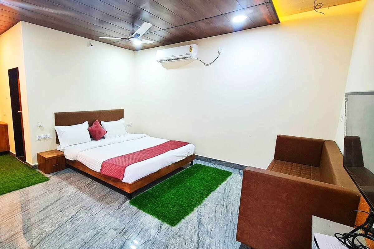 A hotel room with a bed, a desk, a chair, an air conditioning unit, and a ceiling fan.