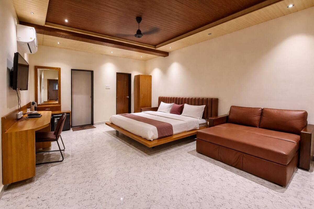 A modern hotel room with a bed, a sofa, a desk, and a mirror.