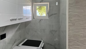 Une salle de bain avec des meubles blancs, une fenêtre intégrée et un plan de toilette blanc surmonté d’un appareil noir.