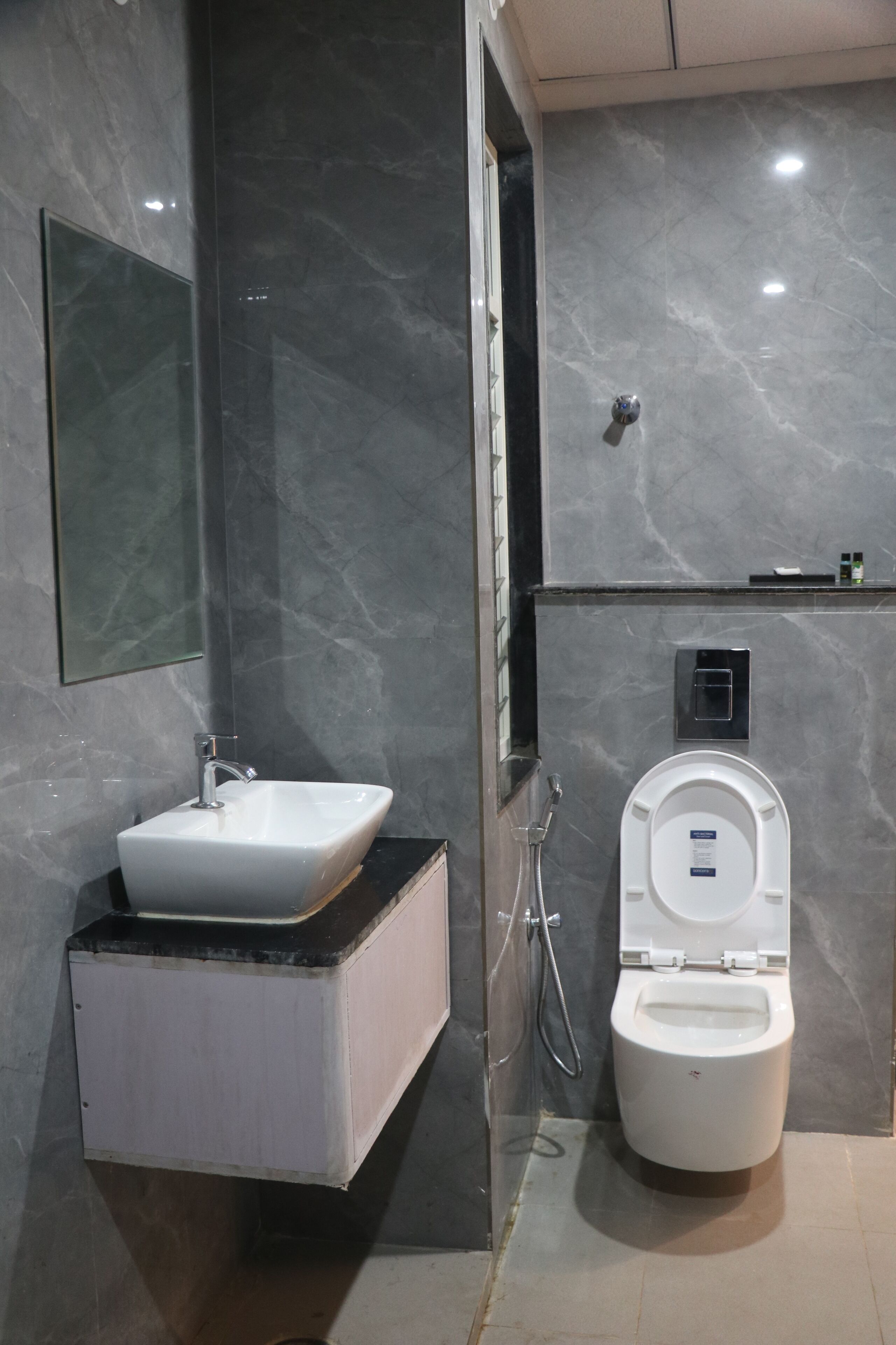 A modern bathroom with a marble wall, a white sink, a toilet, and a mirror.