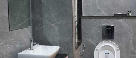 A modern bathroom with a marble wall, a white sink, a toilet, and a mirror.