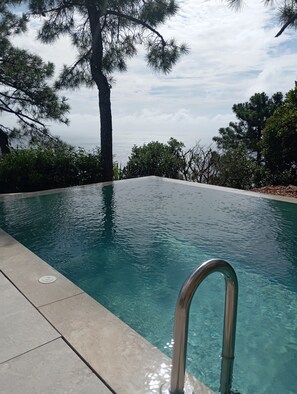 A clear swimming pool with a metal ladder, surrounded by trees and a view of the ocean. - Villa with pool and sea view in an enclosed estate near the sea and the Esterel mountains (Théoule-sur-Mer)