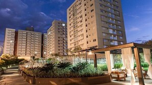 A high-rise residential building complex with multiple apartment buildings, a covered outdoor seating area with plants, and a clear sky. - Evian Thermas Residence by Trul Hoteis (Caldas Novas)