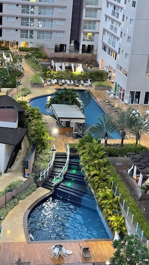 Zona de piscina de varios niveles con una fuente central, rodeada de tumbonas y vegetación.