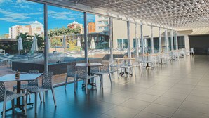 A spacious outdoor cafe with modern metal chairs and tables, large windows offering views of the cityscape. - Evian Thermas Residence by Trul Hoteis (Caldas Novas)