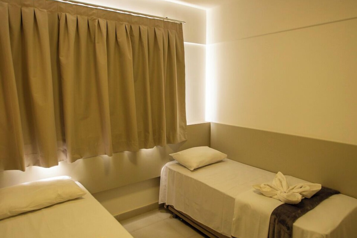 Quarto de hotel com duas camas de solteiro, cada uma com uma almofada e uma toalha.
