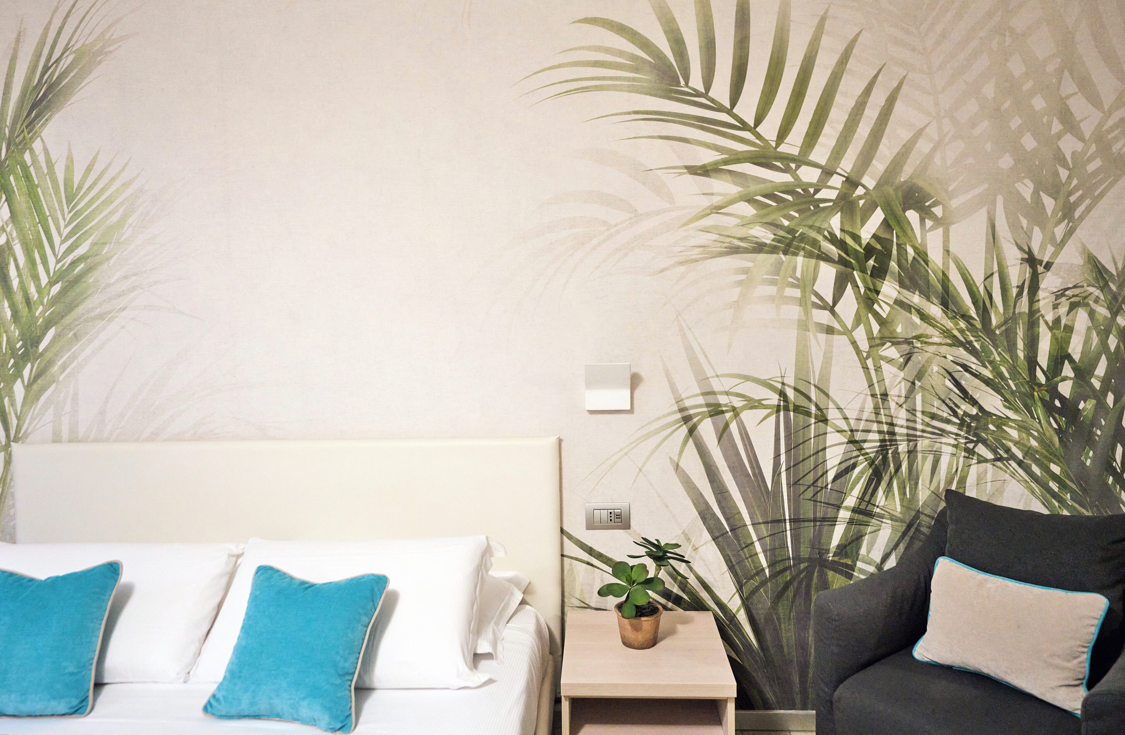 A hotel room with a bed, a nightstand with a plant, and a sofa.