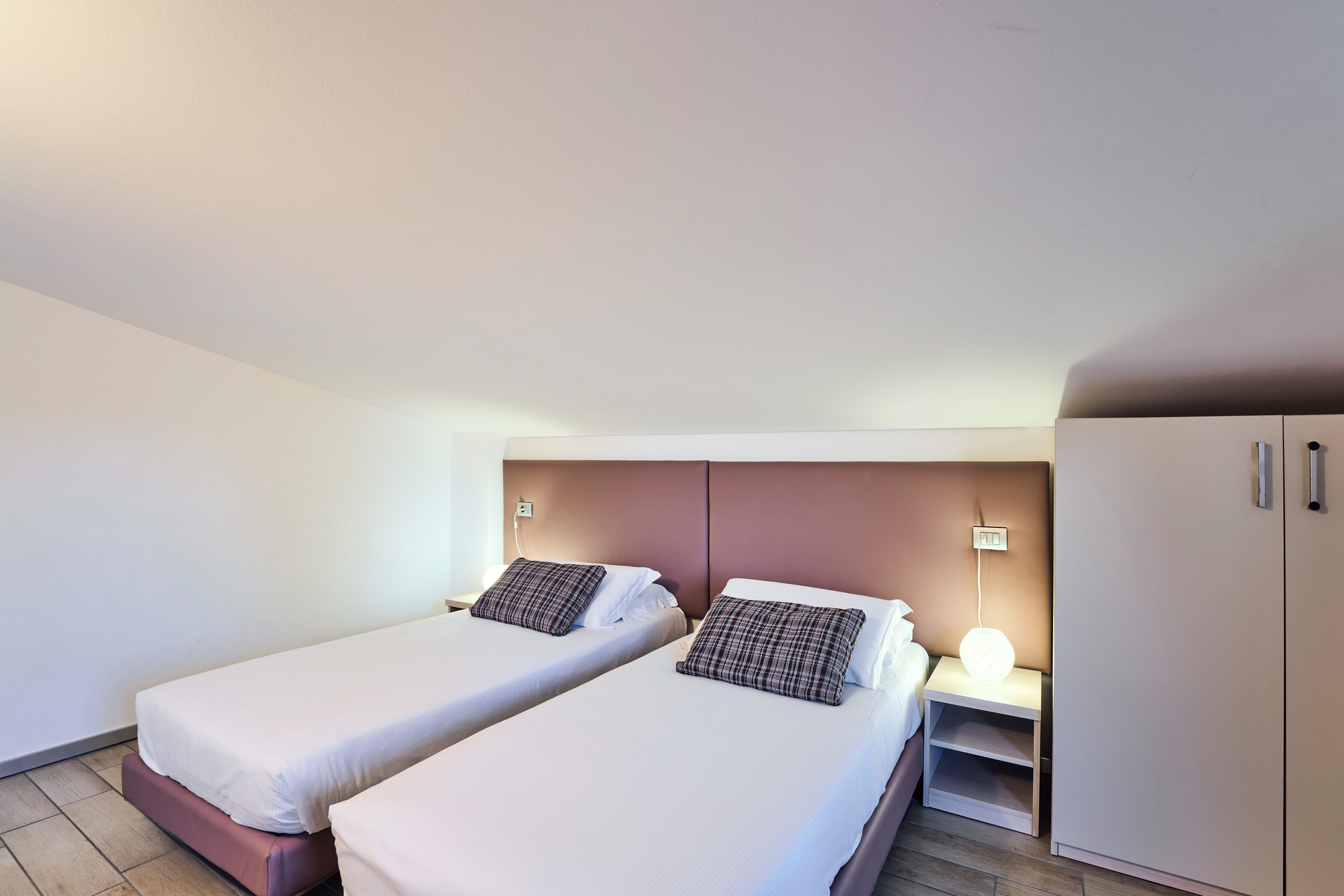 A twin room with two beds, a nightstand with a lamp, and a wardrobe.