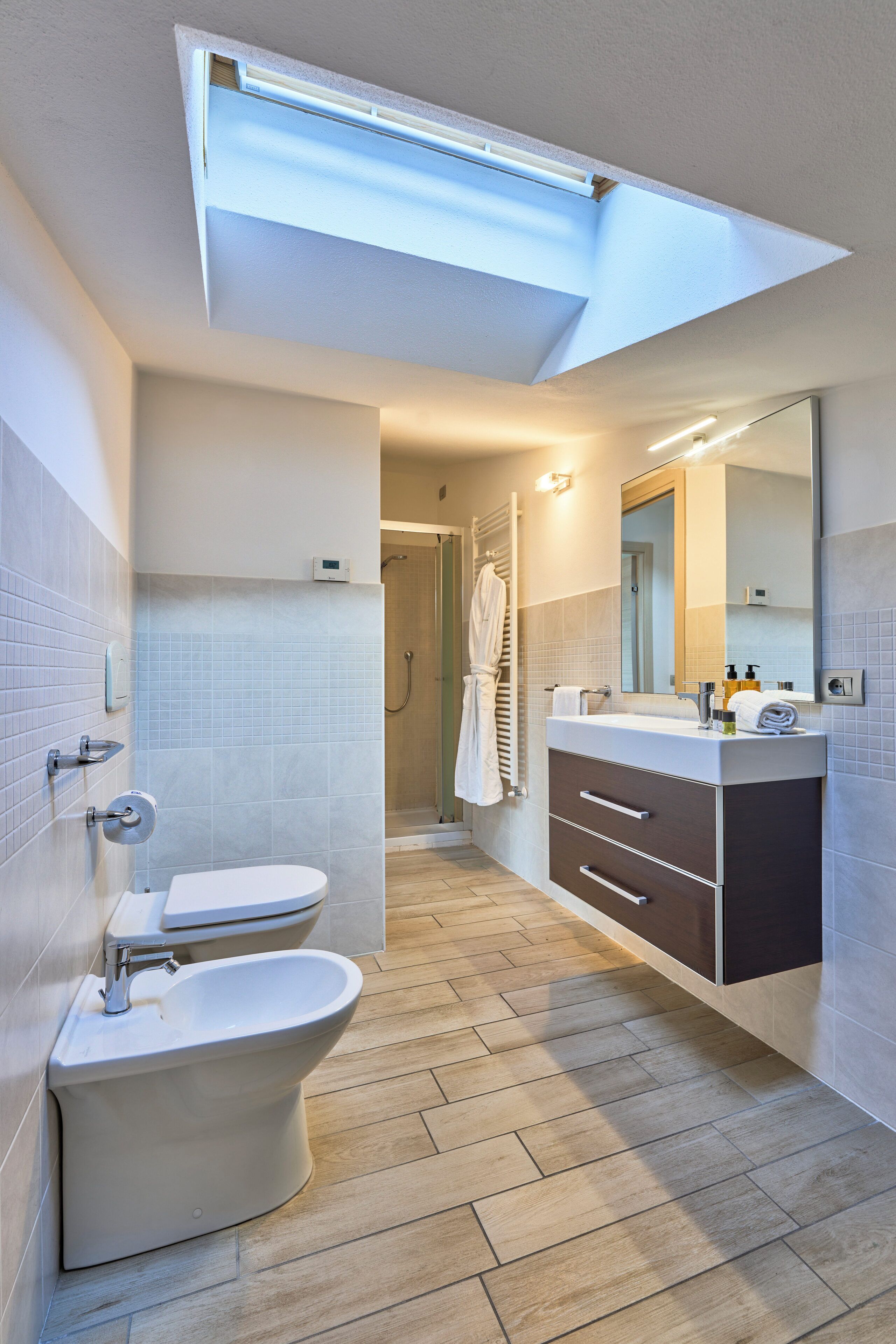 A modern bathroom with a toilet, bidet, vanity with a mirror, and a shower area.