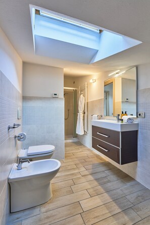 A modern bathroom with a toilet, bidet, vanity with a mirror, and a shower area. - Bellagio Village (Oliveto Lario)