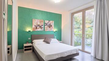 A bedroom with a bed, nightstands, artwork on the wall, and a view through a sliding glass door.