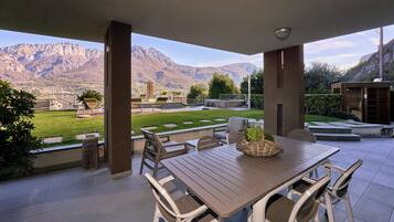 An outdoor patio with a table and chairs, a view of mountains, and a well-maintained lawn.