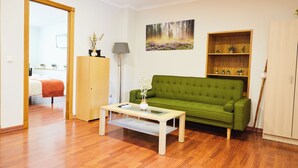 Een woonkamer met een groene bank, een houten salontafel en een schilderij van een bos.