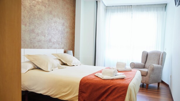 Een hotelkamer met een bed, een stoel, een raam met gordijnen en een structuurwand.