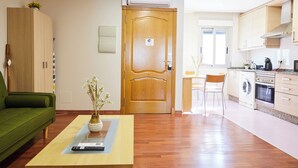 Een modern appartement met een groene bank, een houten deur, een keuken met een wasmachine en een eethoek.