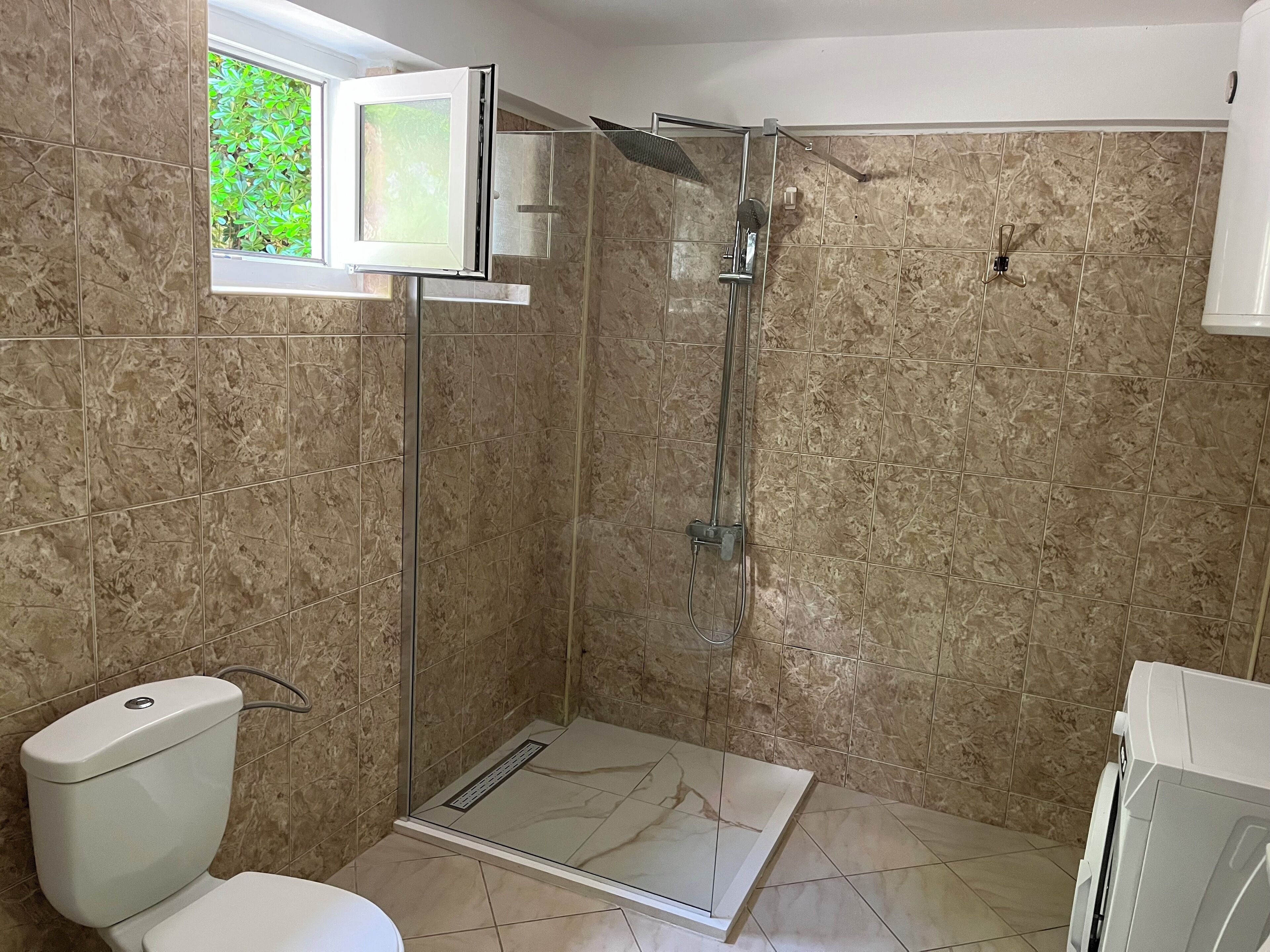 A bathroom with a shower, toilet, and a window.