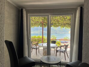 Quarto com uma grande porta de vidro deslizante que dá para uma área externa com mesa e cadeiras, oferecendo vista panorâmica de um lago e montanhas.