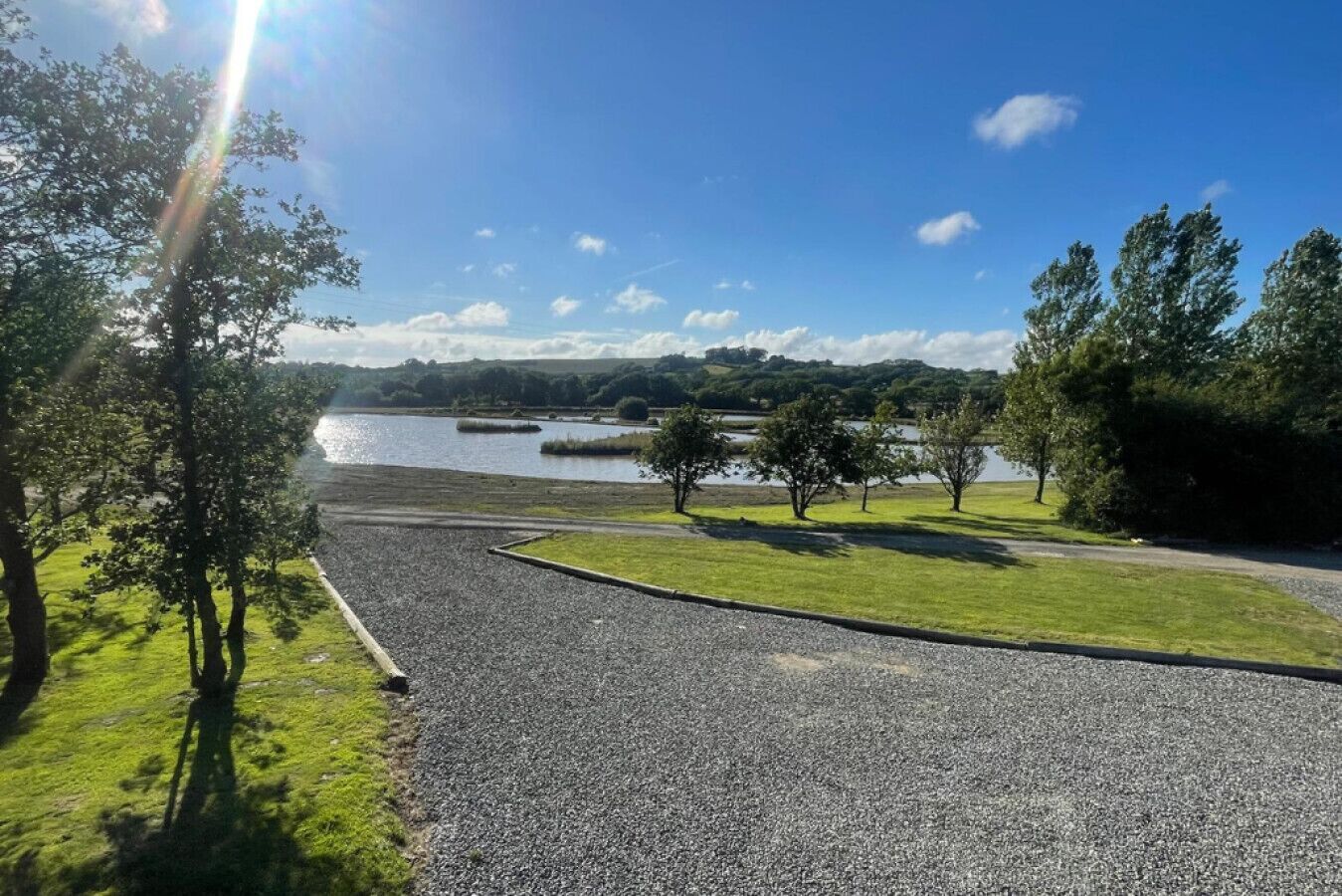 Un’area di parcheggio sterrata con vista su un lago e alberi.