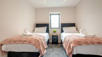 Une chambre d’hôtel avec deux lits, chacun recouvert d’une couvre-lit à motifs floraux roses et agrémenté d’oreillers blancs, une petite table de chevet avec une plante, et une fenêtre donnant sur un paysage agréable.