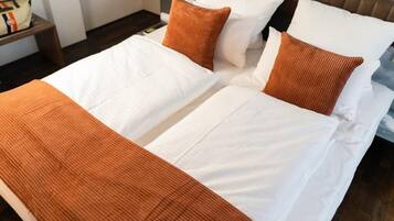 Una cama doble con ropa de cama blanca y naranja, un cabecero de madera y una mesita de noche con un bolso.