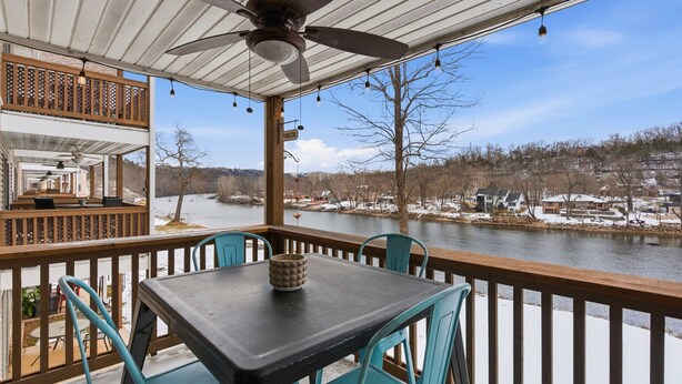 A covered outdoor deck with a table and chairs, overlooking a river and a snowy landscape. - Ashley's Forgetaway For 4 (Branson)