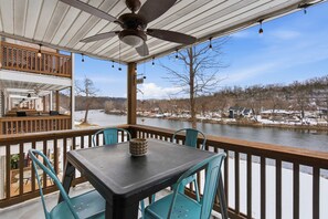 Une terrasse extérieure couverte, dotée d’une table et de chaises, qui offre une vue sur une rivière et un paysage enneigé.