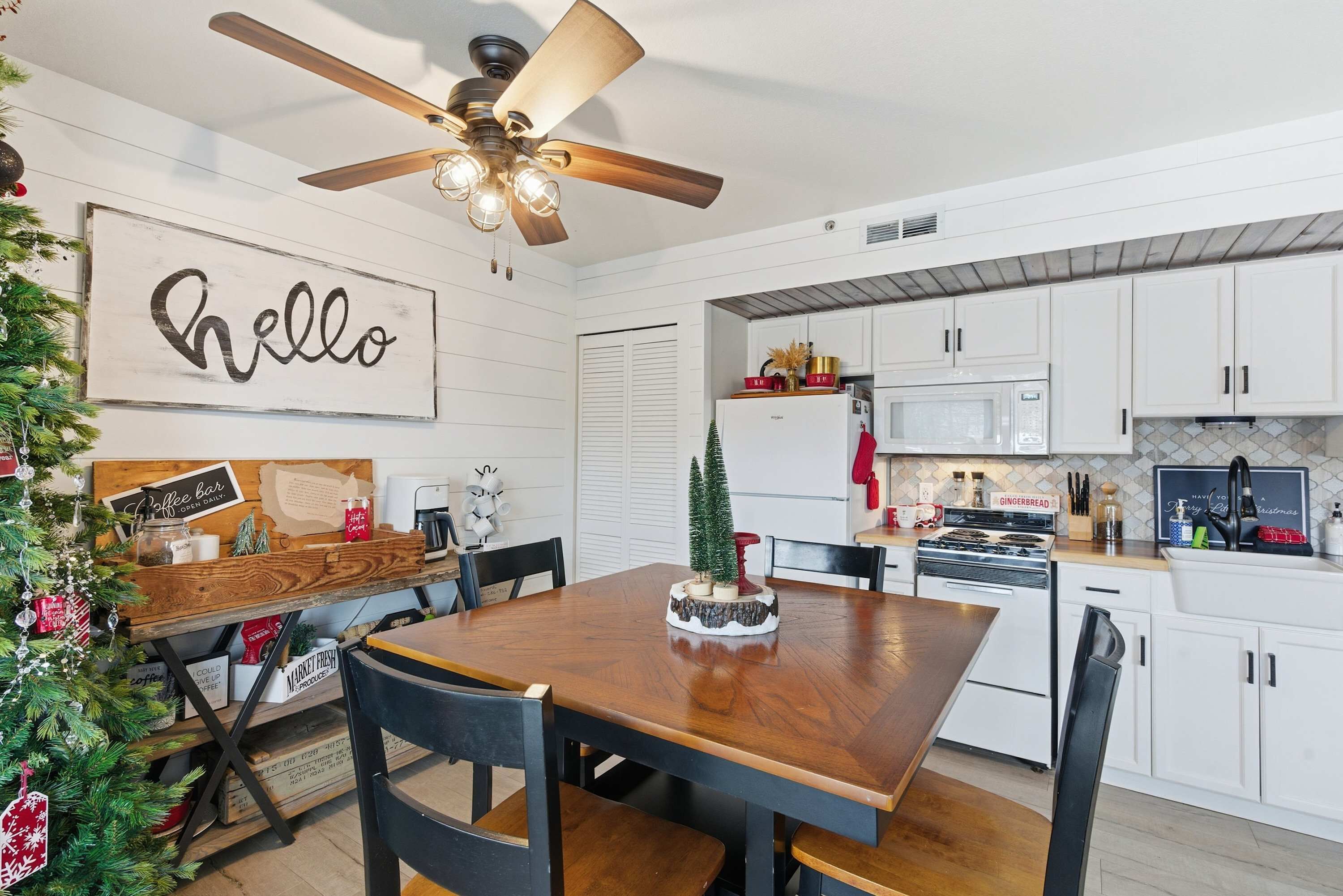 Une cuisine moderne avec des meubles blancs, une table à manger en bois et un ventilateur de plafond.