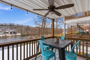 Une terrasse extérieure couverte, dotée d’une table et de chaises, qui offre une vue sur une rivière et des bâtiments.