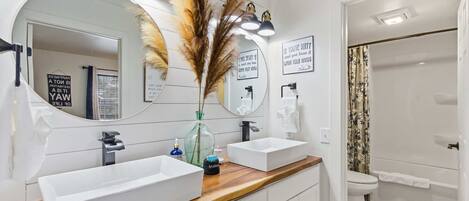 A modern bathroom with two sinks, a large mirror, and a shower.