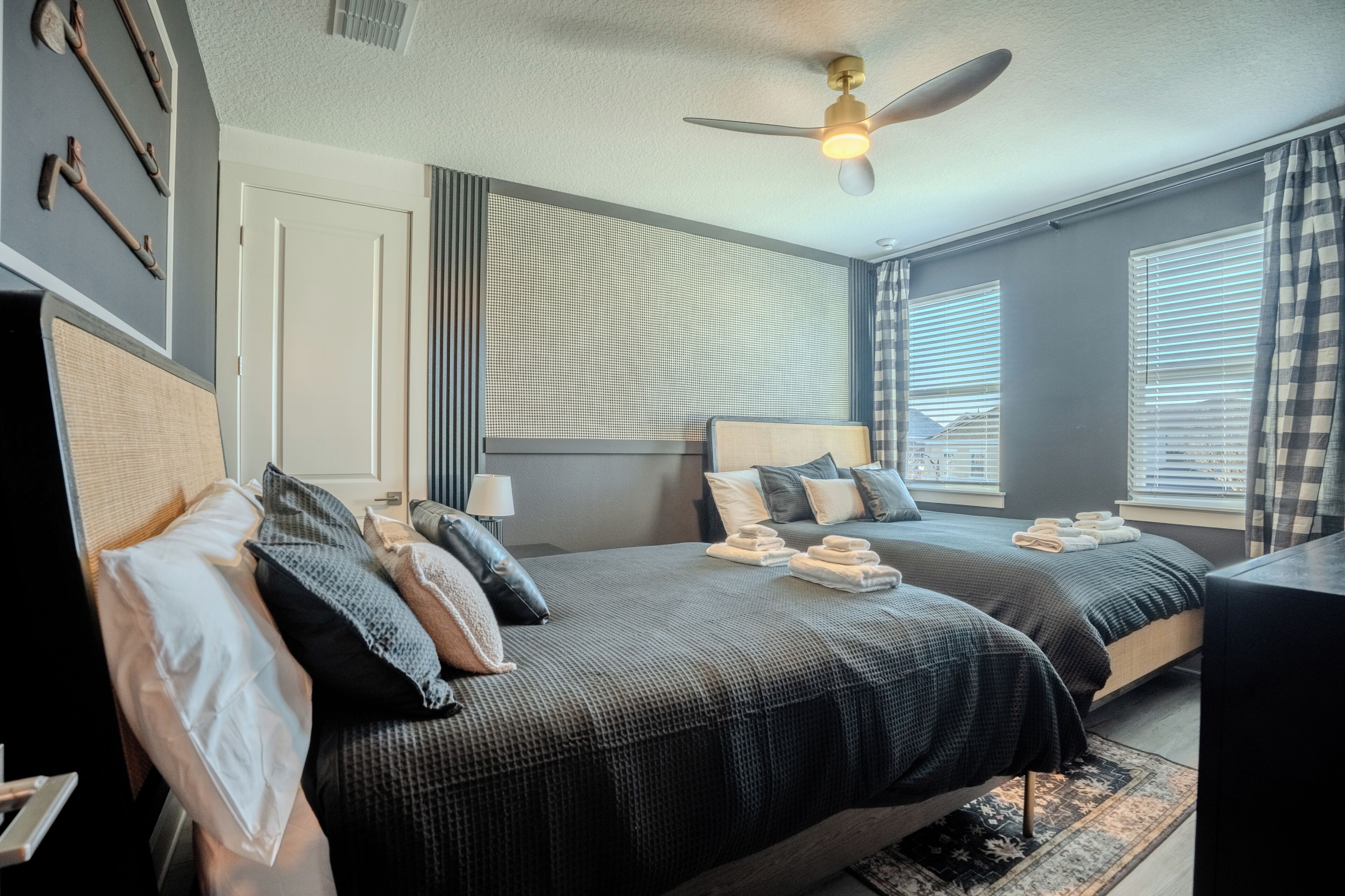 Une chambre d’hôtel avec deux lits, un ventilateur de plafond, une fenêtre avec des stores et une porte.