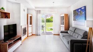 A modern living room with a flat-screen TV, a grey sofa, and a painting of a tropical scene. - Apartment in Baia Village Condominium with Swimming Pool (Albufeira)