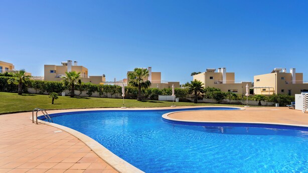 A swimming pool with a tiled deck, surrounded by a well-maintained lawn and palm trees. - Apartment in Baia Village Condominium with Swimming Pool (Albufeira)