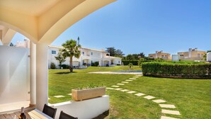 A patio with a table, chairs, and a bottle of wine. There is a well-maintained lawn with a stone path leading to a building. - Apartment in Baia Village Condominium with Swimming Pool (Albufeira)