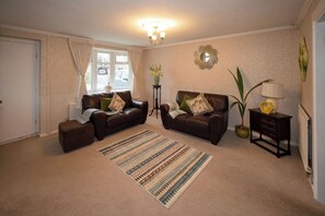 A living room with two leather sofas, a patterned rug, a side table with a lamp, and a decorative wall piece. - 3-Bed Westhoughton | M61 | Parking (Westhoughton)