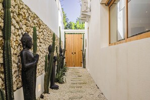 A narrow pathway with a wooden door at the end, flanked by cacti and statues. - Beautiful 4-bedroom villa, special price for the month of March (Bali)