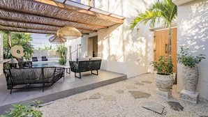 Um pátio externo com piscina, móveis de vime preto e plantas em vasos.
