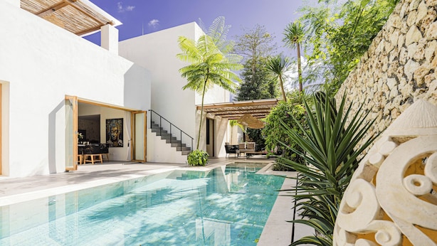 Piscina com parede de pedra e plantas tropicais.
