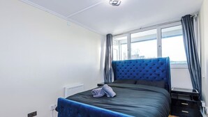 A bedroom with a bed, a nightstand, a window with curtains, and a radiator. - 1-Bed Flat | Hume | 5 Min to MMU & UoM | 15% Off (Greater Manchester)