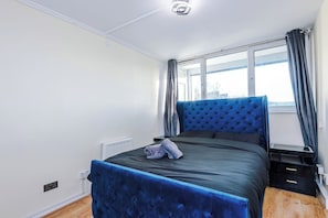 Ein Schlafzimmer mit einem Bett, einem Nachttisch, einem Fenster mit Vorhängen und einer Heizung.