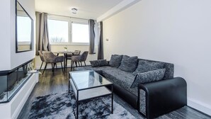 A modern living room with a sofa, coffee table, and dining area with chairs. - 1-Bed Flat | Hume | 5 Min to MMU & UoM | 15% Off (Greater Manchester)