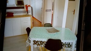 Uma sala de jantar com uma mesa e cadeiras, uma cozinha ao fundo e uma porta que dá para outro cômodo.