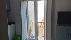 Quarto com porta de correr de vidro que dá para área externa, máquina de lavar, lixeira verde e televisão sobre suporte.