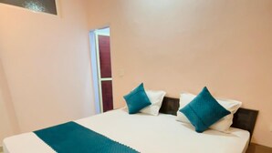 Una cama bien hecha con una colcha color turquesa y almohadas, un cabecero de madera y una pared lisa con una ventana pequeña.