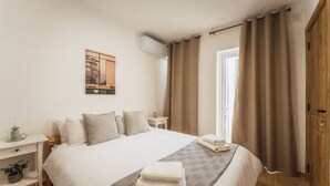 A neatly arranged hotel room with a large bed, a bedside table with a lamp, a wall-mounted air conditioner, and a window with curtains. - Gozo Penthouse With Terrace BBQ Private Roof (Xaghra)