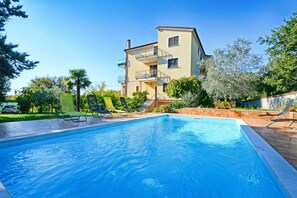 A swimming pool with lounge chairs, a multi-story building with balconies, and surrounding greenery. - Apartment With Pool Near Kanegra Beach (Umag)