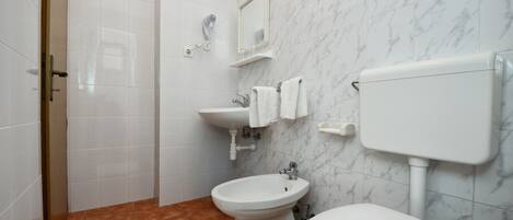 A bathroom with a toilet, bidet, sink, and a mirror.